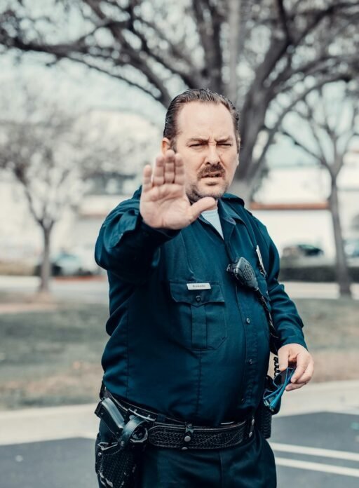 A male police officer in uniform extends his arm to direct traffic in an outdoor setting.
