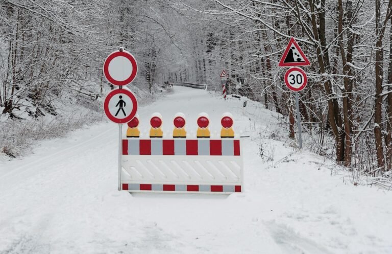 A snow-covered road flanked by trees with warning signs indicating a path closure in winter.